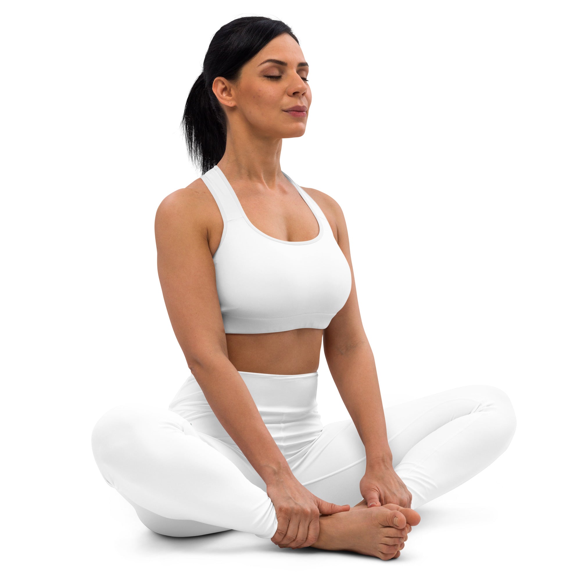 Woman in a white sports bra and leggings sitting cross-legged on a white background