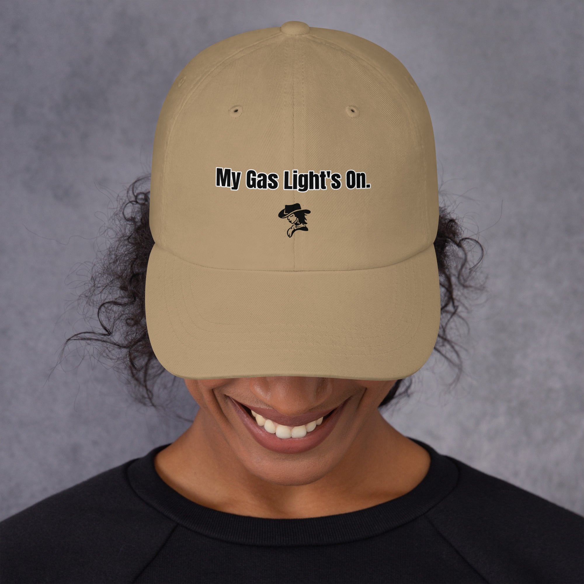 Person wearing a beige cap with 'My Gas Light's On.' text on a gray background