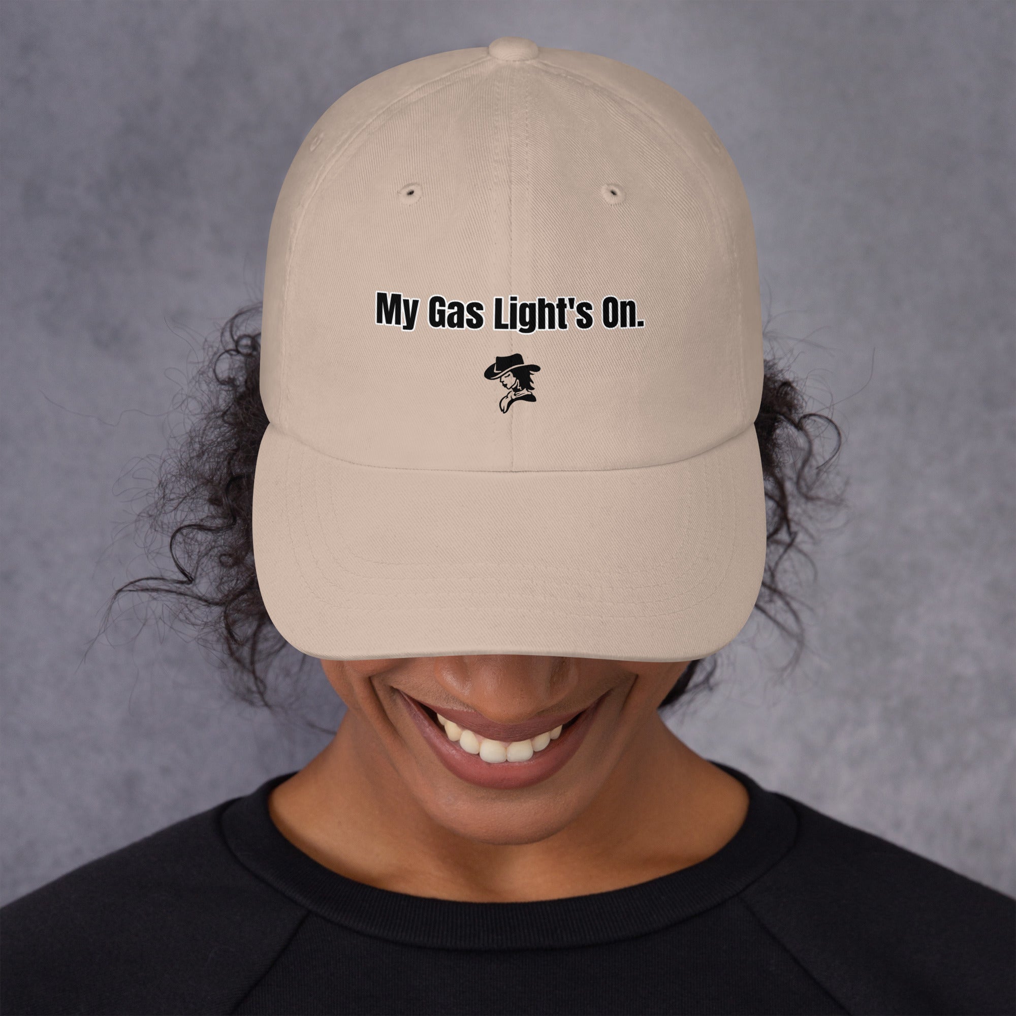 Person wearing a beige cap with 'My Gas Light's On.' text on a gray background